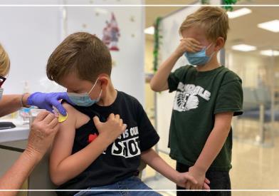 boy gets his vaccine while his brother holds his h